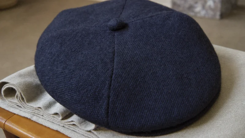 Coppola in tweed spigato blu navy su tessuto di lino piegato