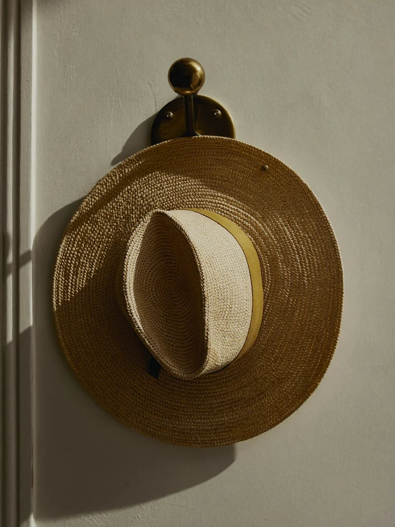 Cappello di paglia naturale a tesa larga appeso a un gancio d'ottone